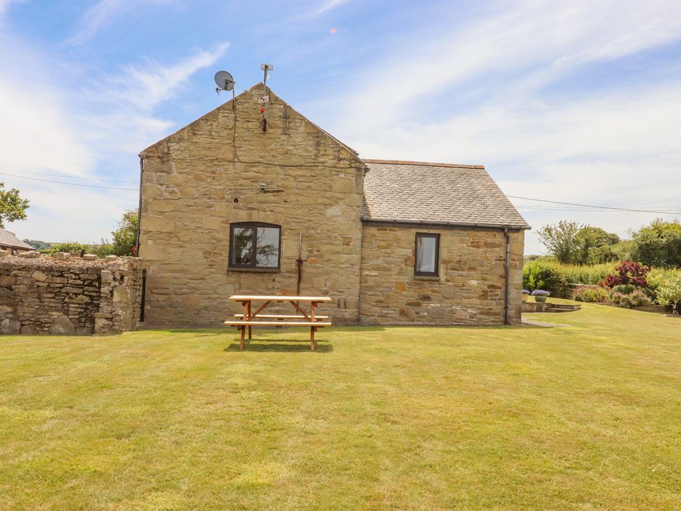 A stone building with two windows and a picnic bench on a lawn at The Cottage @ Picton near Gwespyr