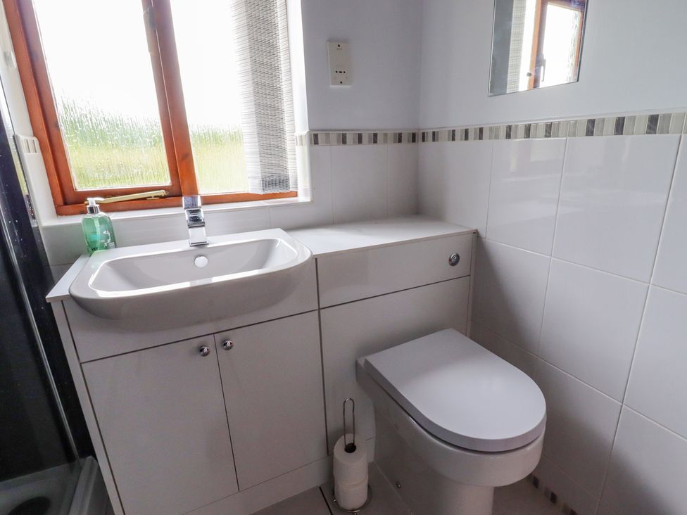 A bathroom with a sink, toilet, window, mirror, and white cabinetry at The Cottage @ Picton near Gwespyr