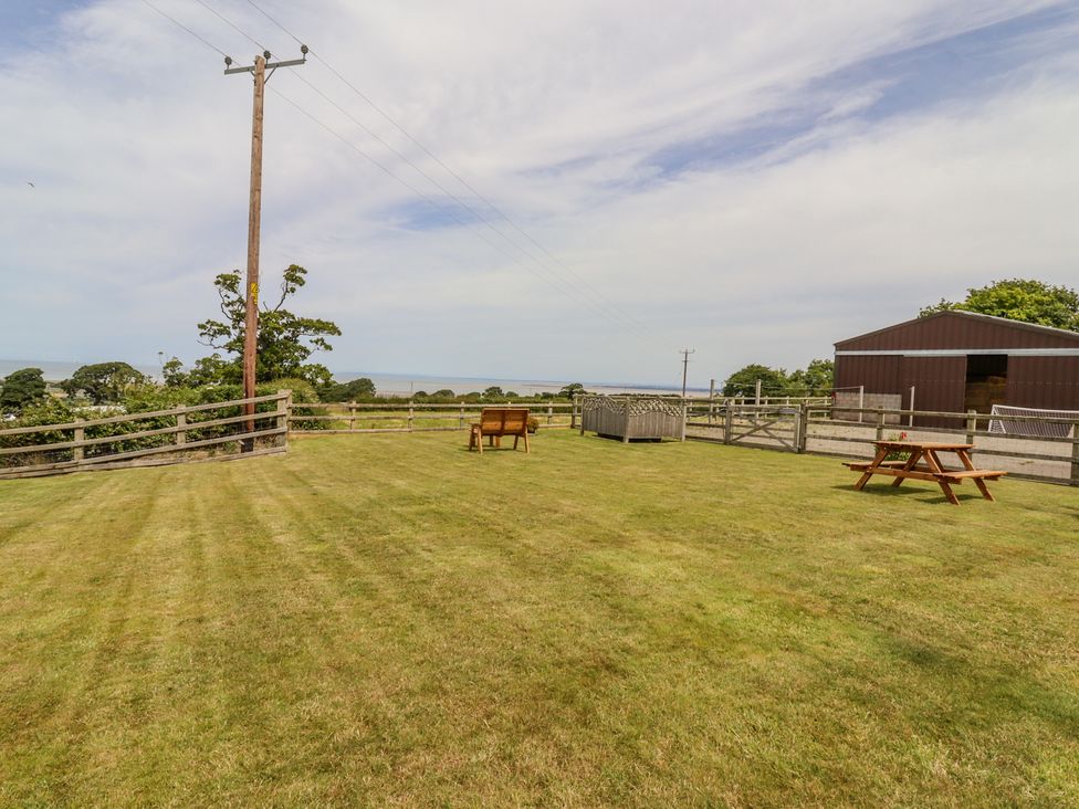 A fenced grassy yard with a wooden bench and picnic table near a barn at The Cottage @ Picton near Gwespyr