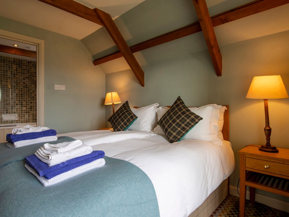 A bedroom with a double bed two bedside tables with lamps and folded towels at Quarryfield in Munlochy