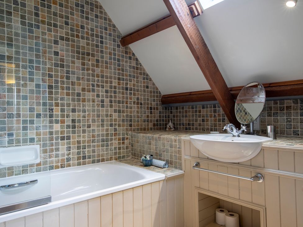 A bathroom with a bathtub sink tiled walls and exposed wooden beams at Quarryfield in Munlochy