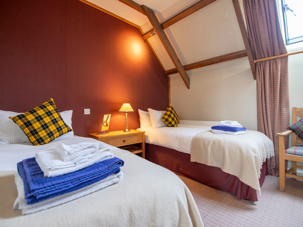 A bedroom with two single beds pillows folded towels bedside lamp and wooden chair at Quarryfield in Munlochy