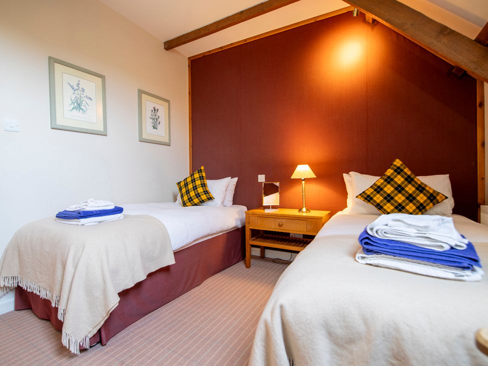 A bedroom with two single beds a wooden nightstand and a lamp at Quarryfield Munlochy