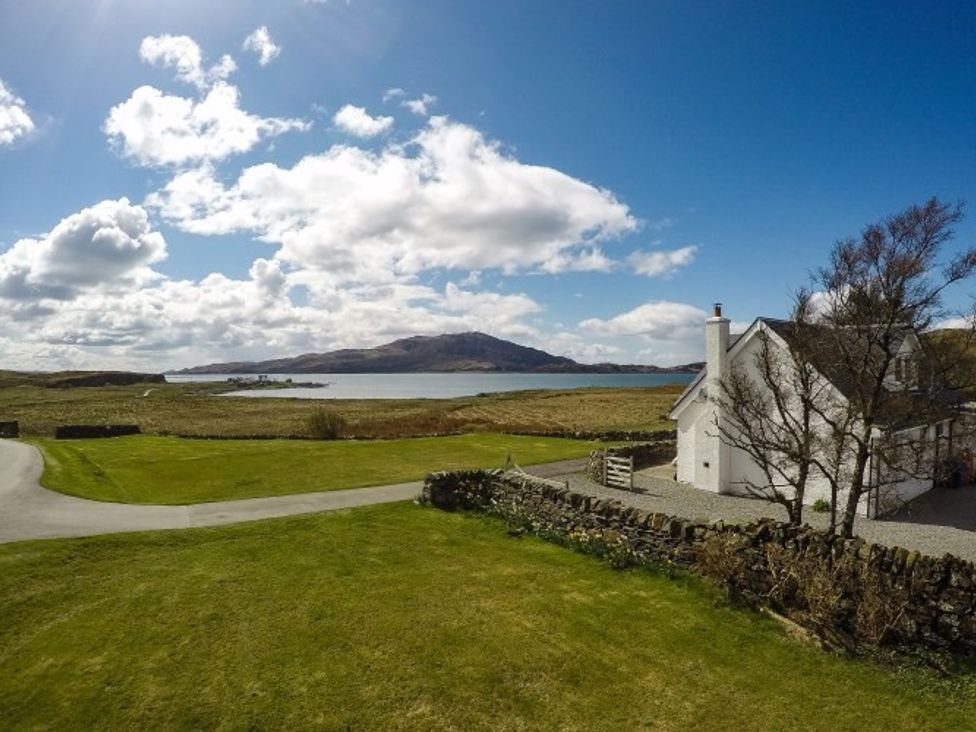 A grass lawn with a stone wall and a white house near a body of water with hills in the background at Ardlarach Lodge in Cullipool Isle Of Luing