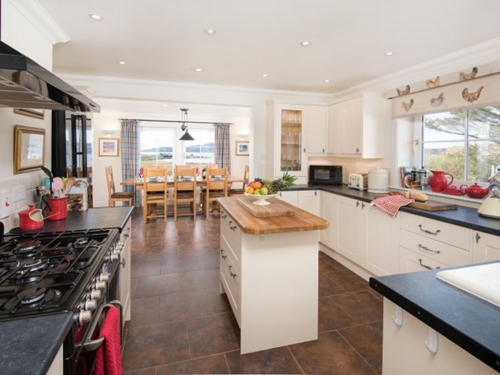 A kitchen with a cooking range island and dining table at Ardlarach Lodge in Cullipool Isle Of Luing