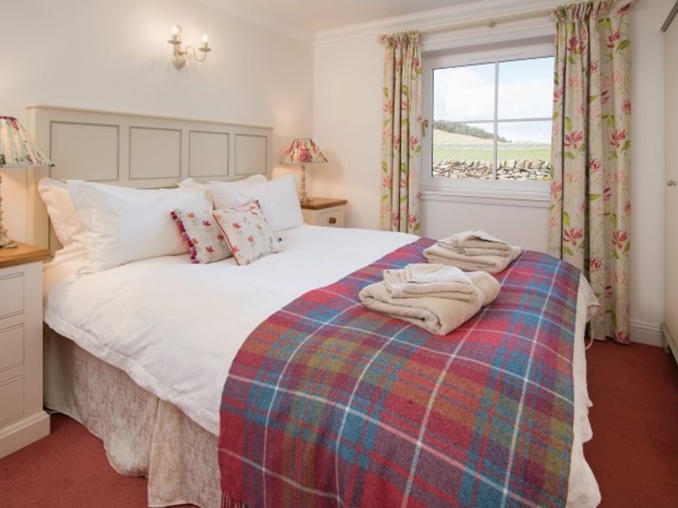 A bedroom with a double bed covered with white bedding and a red plaid blanket at Ardlarach Lodge in Cullipool Isle Of Luing