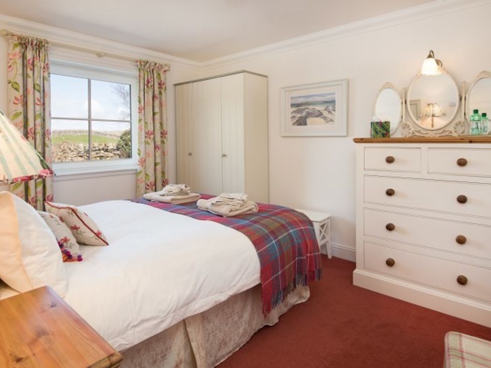 A bedroom with a bed covered with white linens and a tartan blanket a wardrobe and a dresser with mirrors at Ardlarach Lodge in Cullipool Isle Of Luing
