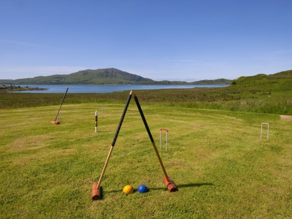 A grassy lawn with croquet equipment including mallets, balls, and wickets with hills and a body of water in the background at Ardlarach Lodge Cullipool Isle Of Luing