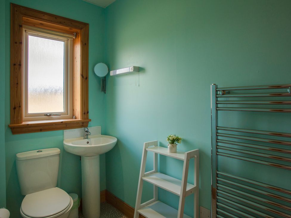 A bathroom with a toilet sink small white shelf and towel rack at Rockpool Glendale Isle of South Uist