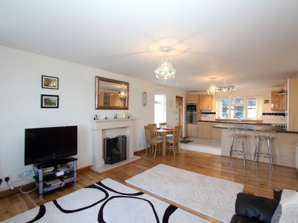 An open plan living room and kitchen with a fireplace television dining table and bar stools at Eriskay Views Cottage in Eriskay