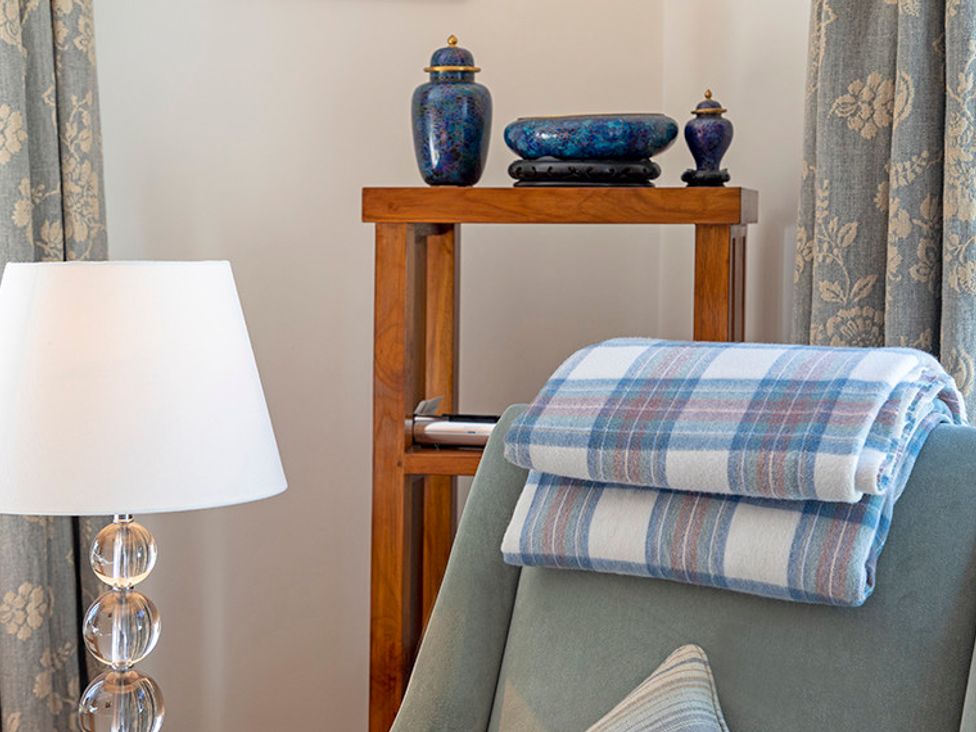A corner with a lamp beside a chair with a folded blanket on the back and a wooden shelf with decorative blue pottery at Mullach Ruadh in Glenfinnan near Corpach