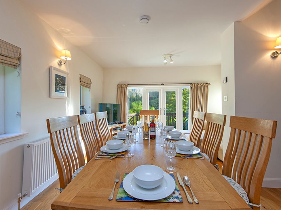 A dining room with a wooden table set for eight with plates bowls and glasses at Mullach Ruadh in Glenfinnan near Corpach