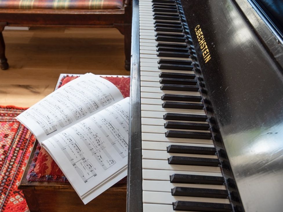 A piano keyboard with sheet music on a cushioned wooden bench at Beltie Lodge in Borgue