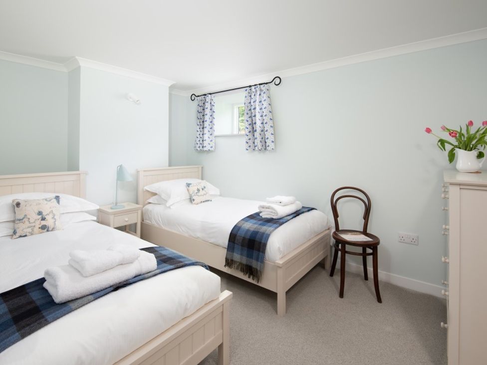 A bedroom with two single beds a small nightstand and lamp a wooden chair and a dresser with flowers at Beltie Lodge in Borgue