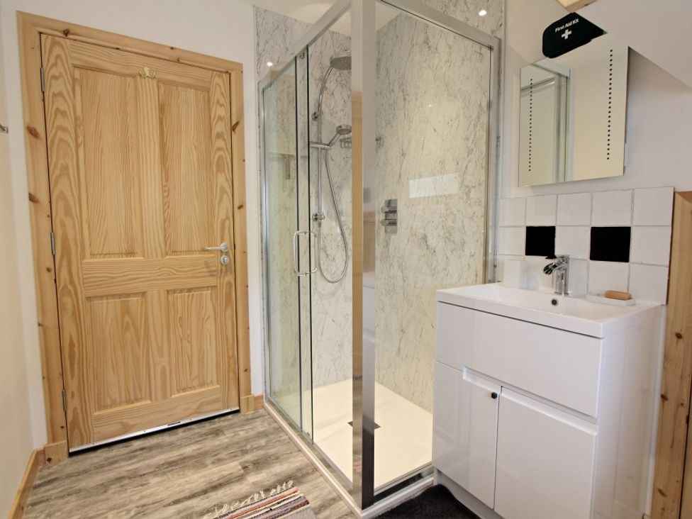 A bathroom with a wooden door a glass shower enclosure and a white sink with a mirror above at Taigh Eachainn in Valtos near Timsgearraidh