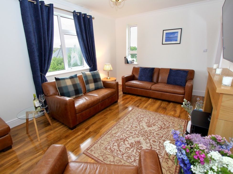 A living room with brown leather sofas a patterned rug blue curtains and flowers at Tulloch House in Lochboisdale