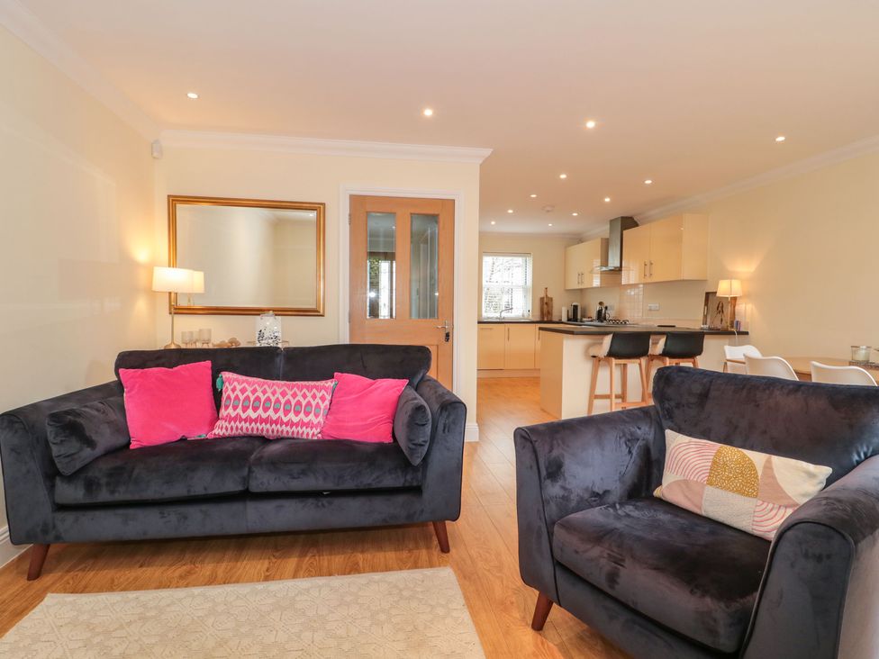 A living room with two dark sofas with pink and patterned cushions a wooden floor and an open kitchen area at 9A Wick Lane in Christchurch
