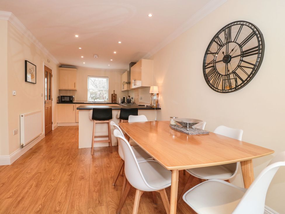 A kitchen and dining area with wooden flooring a wooden dining table white chairs a large wall clock and kitchen cabinets at 9A Wick Lane in Christchurch