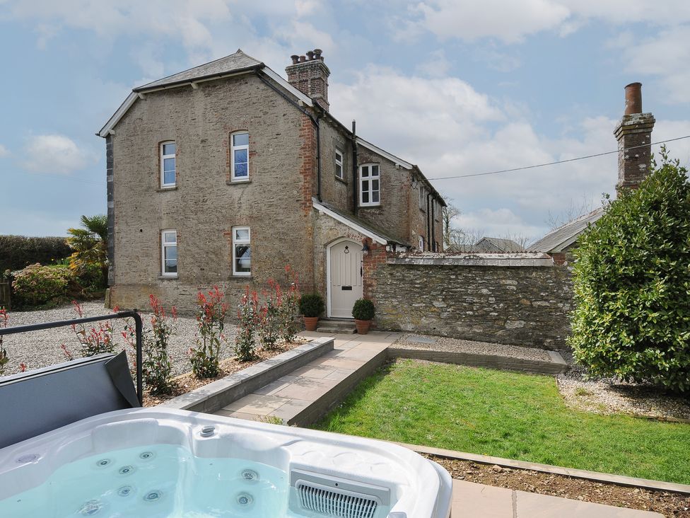 An outdoor view of a stone house with a garden, hot tub, plants, and a stone wall at Skylarks in No Man's Land near Looe