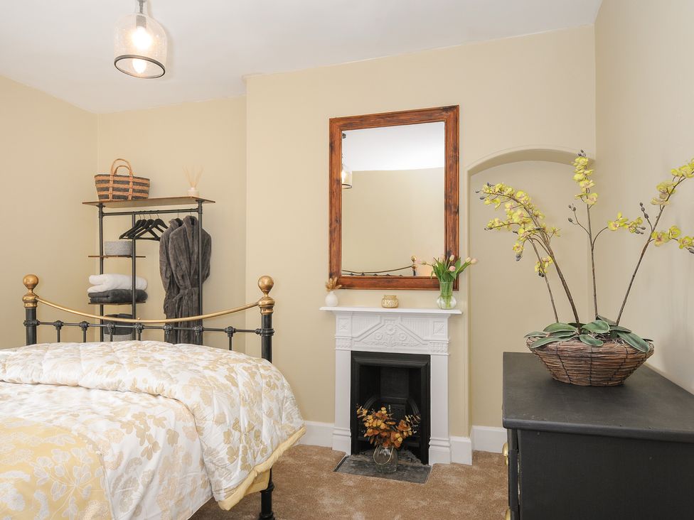 A bedroom with a metal bed a mirror above a fireplace and a plant on a dresser at Skylarks in No Mans Land near Looe