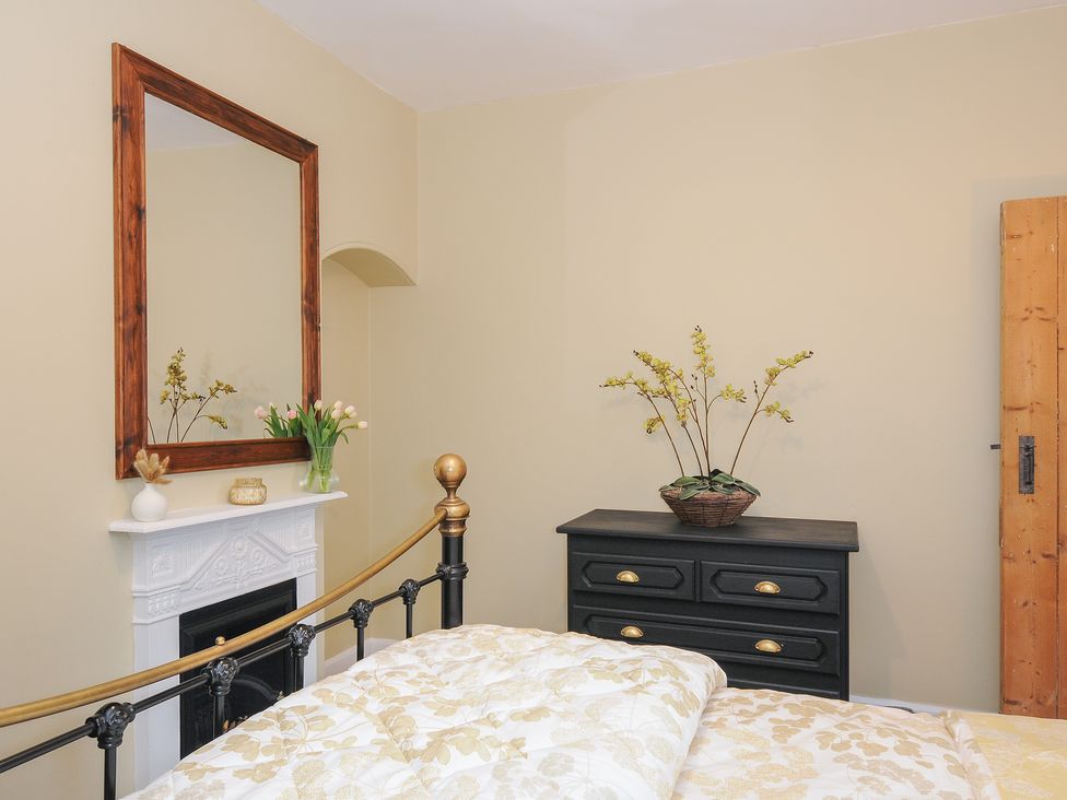 A bedroom with a bed a white fireplace with a mirror above and a black chest of drawers with a plant at Skylarks in No Mans Land near Looe