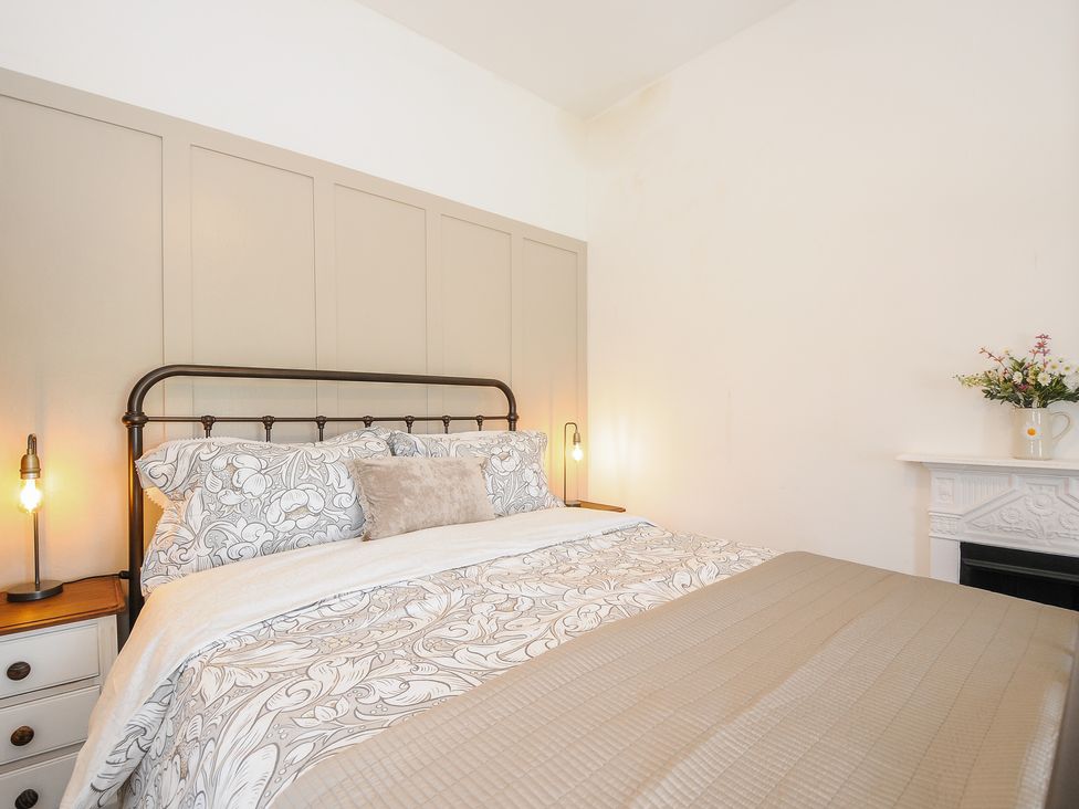 A bedroom with a bed that has patterned bedding two bedside tables with lamps and a white fireplace with flowers at Skylarks in No Man's Land near Looe
