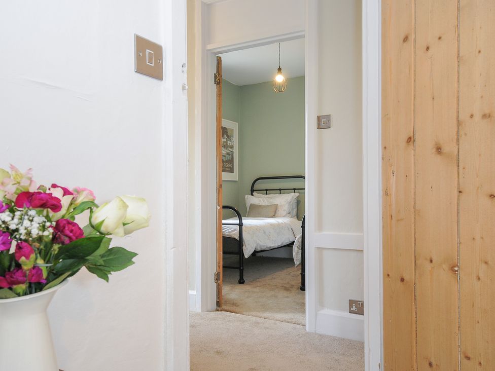 A hallway leading to a bedroom with a metal bed frame and a hanging light at Skylarks in No Mans Land near Looe
