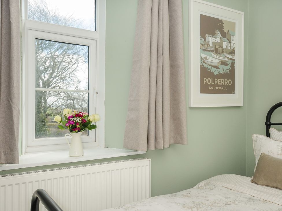 A bedroom corner with a window a vase of flowers beige curtains and a framed Polperro Cornwall poster at Skylarks No Mans Land near Looe