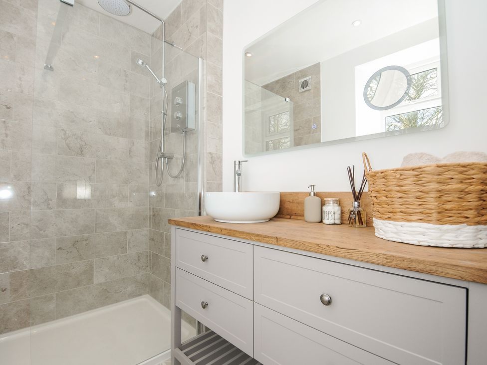 A bathroom with a walk in shower and a wooden countertop with a sink and toiletries at Skylarks in No Man's Land near Looe