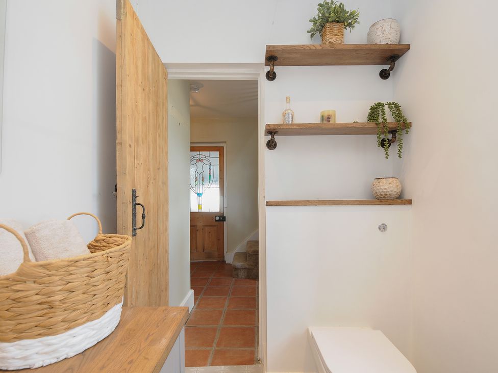 A bathroom with wooden shelves holding plants and candles and a wooden door leading to a hallway with tiled floor at Skylarks in No Mans Land near Looe