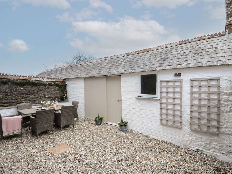 A courtyard with a dining table and chairs on gravel next to white brick walls and a stone wall at Skylarks in No Man's Land near Looe
