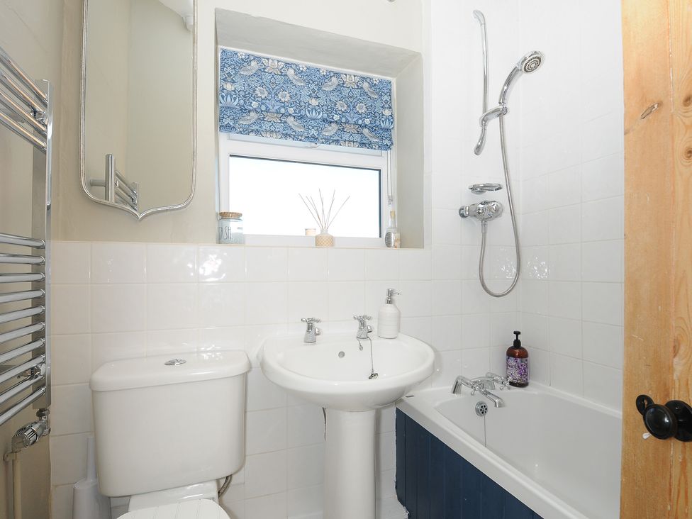 A bathroom with a toilet sink bathtub shower and a window with a blue patterned blind at Skylarks in No Mans Land near Looe