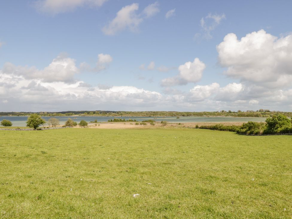 An open green field with trees and water in the background under a partly cloudy sky at Cartron Cottage Ballintubber County Mayo