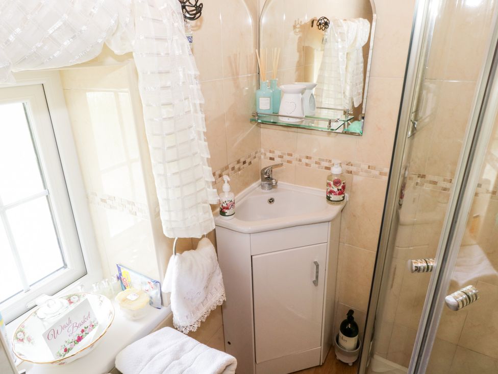 A small bathroom corner with a white sink cabinet a mirror glass shower and window at Cartron Cottage Ballintubber County Mayo