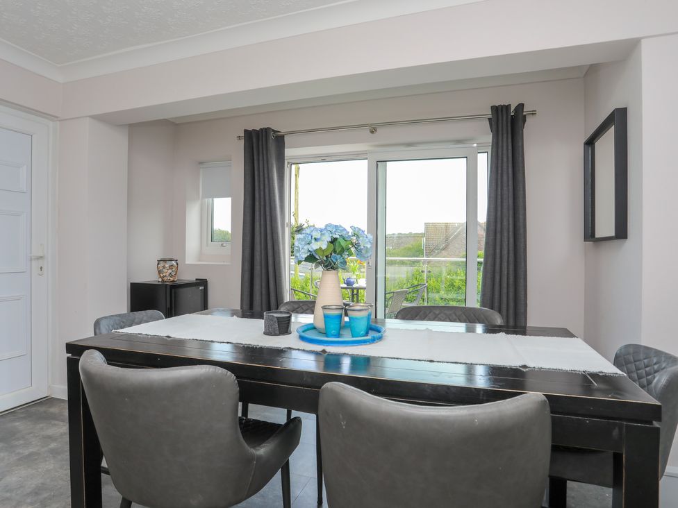 Dining area with black table and gray chairs and a vase of flowers on the table at Swn Y Mor in Benllech