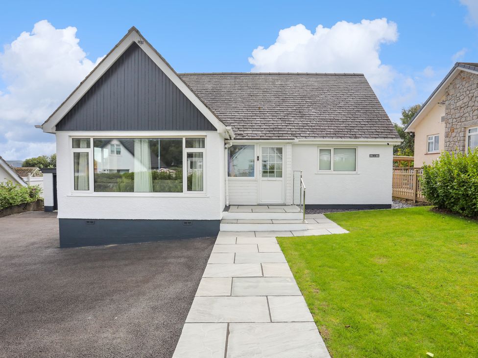 A white house with a dark roof and a paved walkway leading to the front door with grass on one side at Swn Y Mor in Benllech