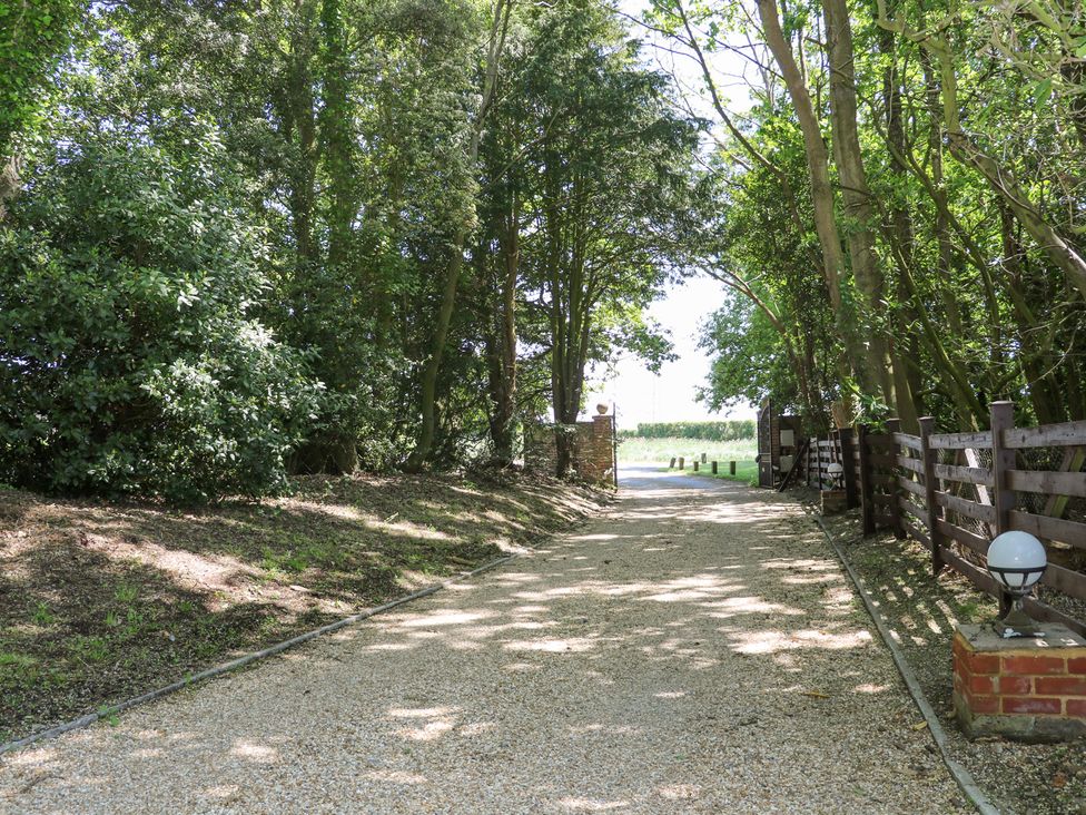 A gravel driveway lined with trees and a wooden fence with lamps at Robins Nest in Titchfield Common