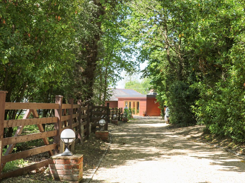 A gravel driveway lined with wooden fences and garden lamps leading to a house surrounded by trees at Robins Nest in Titchfield Common