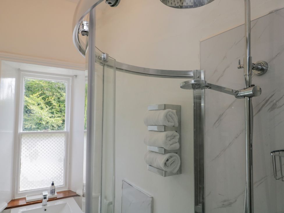 A bathroom with a glass shower enclosure white towels on a rack and a window with frosted film at The Residence in Cleator