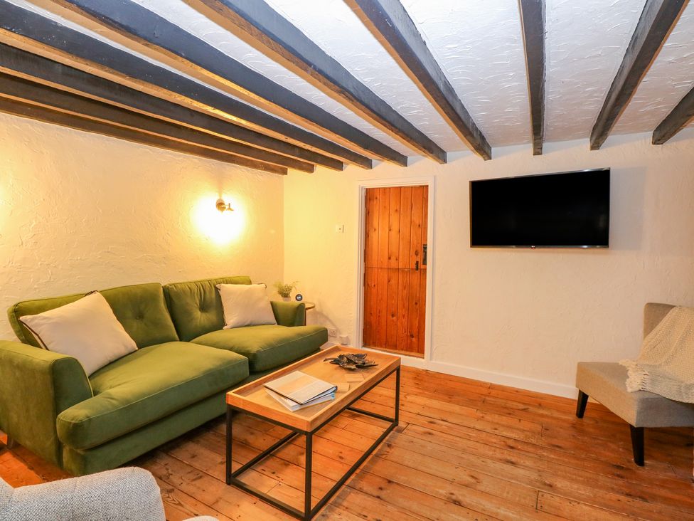 A sitting room with a green sofa white cushions a wooden door a wall mounted TV and a wooden coffee table at Vintner's Cottage Freethorpe near Reedham
