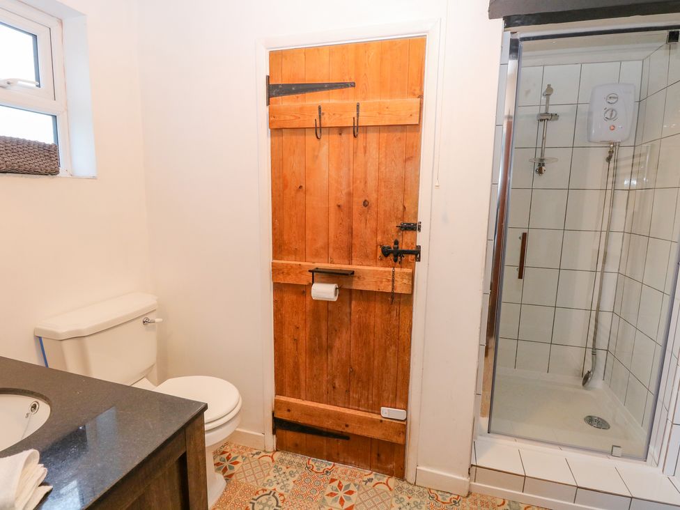 A bathroom with a toilet sink wooden door and a glass shower enclosure at Vintner's Cottage in Freethorpe near Reedham