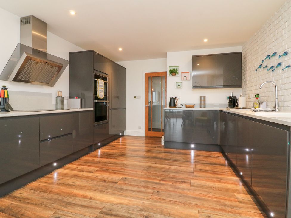 A kitchen with dark cabinets wooden floor and a stainless steel extractor hood at 1 Cheyne Beach Apartments in Ilfracombe