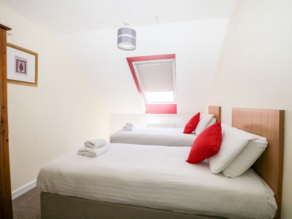 A bedroom with two single beds with white linens and red pillows under a slanted ceiling window at Flat 34 - Marine Court in Littlehampton
