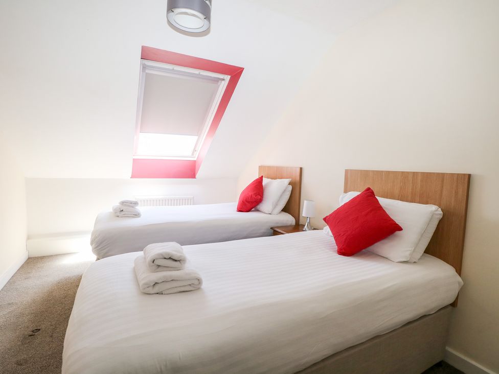A bedroom with two single beds white bedding red pillows and a skylight window at Flat 34 - Marine Court in Littlehampton