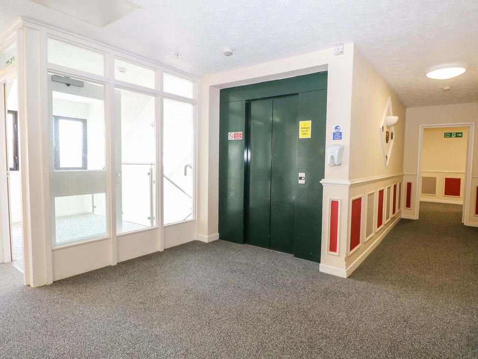 A hallway with a green elevator door next to a glass stairwell and a corridor at Flat 34 - Marine Court in Littlehampton