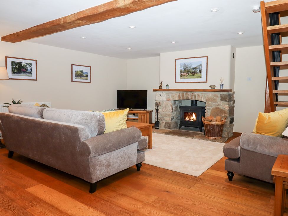 A living room with sofas a stone fireplace with a wood burning stove a television and wooden flooring at Little Orchard in Ashburton Down near Ashburton