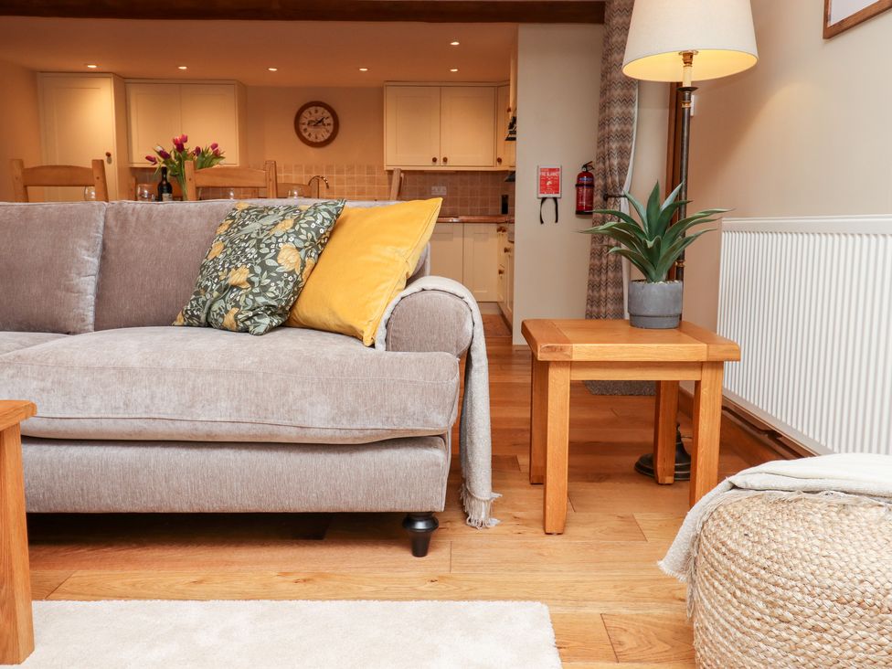 A sofa with cushions and a throw next to a wooden side table with a plant and a lamp in a living area at Little Orchard in Ashburton Down near Ashburton