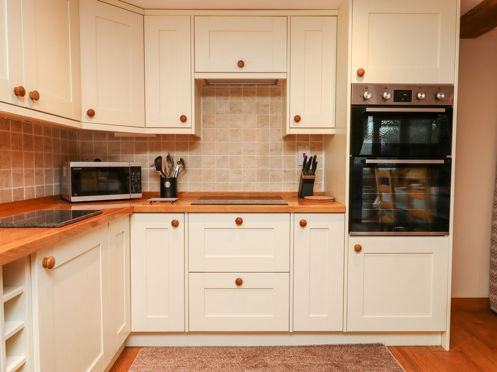 A kitchen with white cabinets wooden countertops a microwave oven built-in oven utensils and a knife block at Little Orchard in Ashburton Down near Ashburton