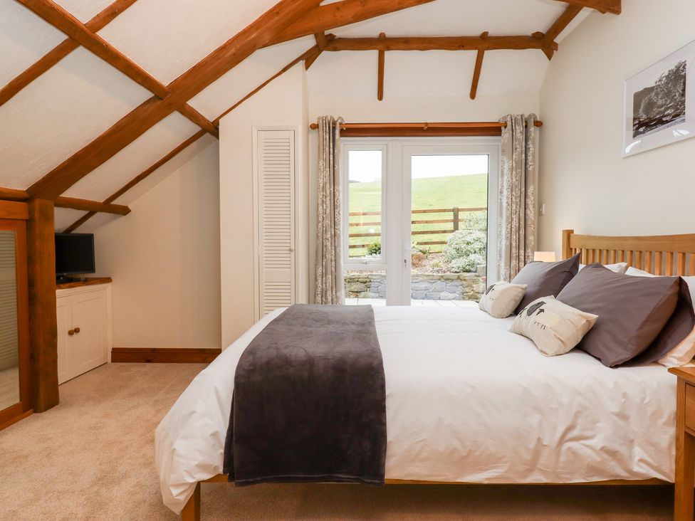 A bedroom with a wooden bed and gray pillows near glass doors with a view of a garden at Little Orchard in Ashburton Down near Ashburton
