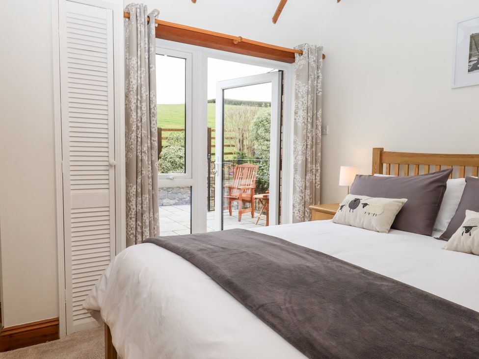 A bedroom with a wooden bed and cushions next to glass doors leading to a patio at Little Orchard in Ashburton Down near Ashburton